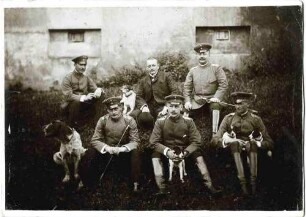 Offiziere (sechs Personen) des Regiments im Garten des Offizierskasinos in Wiblingen, teilweise in Uniform auf dem Boden sitzend, zwei Hunde
