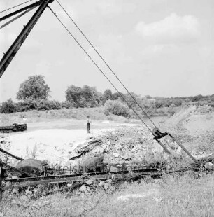 Kremerberg: Müllgrube: Arbeiter mit Schaufel: im Vordergrund verrostete Teile von Kranbagger: hinten Wassertümpel