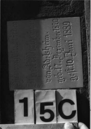 Grabstein 15 (Index: 100079837) Material: Sandstein, weiße Marmorplatten Zustand: beschädigt, Sockel verwittert Maße HxBxT: 196x65x30 cm Beschreibung: ädikulaartige Stele mit Säulen, getreppter Sockel, giebelartiger Abschluß mit Eckakroteren, zwei rechteckige Schriftplatten Symbolik: Blüten, Ranken: Grabstein 15C