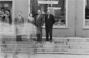 Niesky. Mehrere Personen (Lehrer oder Dozenten ?) auf den Stufen vor einem HO-Industriewarenladen "Foto - Optik"