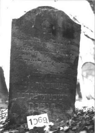 Grabstein 1069 (Index: 99899702) Material: Sandstein Zustand: angewittert Maße HxBxT: 114x64x11 cm Beschreibung: Stele mit Konvexbogenabschluss, im Bogenfeld segnende Hände (Priestersegen) Symbolik: segnende Hände (Priestersegen) Besonderheit: kulturhistorisch wertvoll / hist.-wiss. Gründe (Gemeindestellung): Grabstein 1069