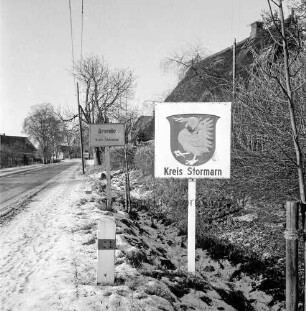 Ortseingang mit Ortsschild im Hintergrund: vorn Grenze zum Kreis Herzogtum Lauenburg: Schild mit Kreiswappen Stormarn-Schwan: Winter