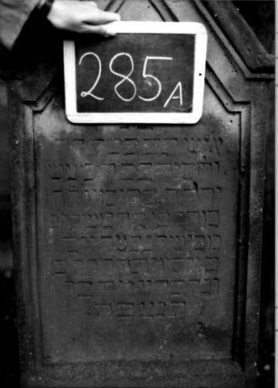 Grabstein 285 (Index: 100111003) Material: Sandstein Zustand: verwittert Maße HxBxT: 134x57x19 cm Beschreibung: Stele, getreppter Sockel, giebelartiger Abschluß, rechteckig erhöht, Schriftfeld eingetieft Symbolik: segnende Hände: Grabstein 285A