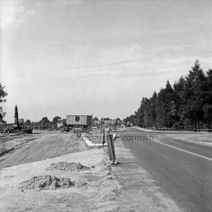 Straßenbau: Ausbau der Kreuzung von Landesstraße zwischen Stapelfeld und Großensee und Straße von Stellau zur Alten Landstraße: linke Fahrspur und Verkehrsinseln in Bau, Vorbereiten des Untergrunds: Baustellensicherung mit Warnbaken und Flatterband, Verkehrsschilder: vorne Sandhaufen: Lkw: links Fahrbagger, Nivelliergerät: hinten Baufahrzeug: hinten rechts Bäume: im Hintergrund Bäume, Haus