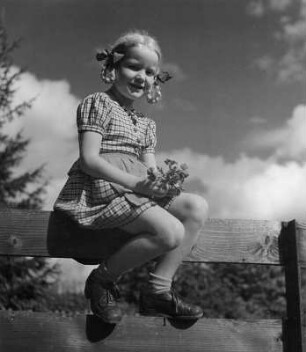 Kinderbilder. Porträt eines kleinen Mädchens mit Affenschaukelfrisur, auf einem Koppelzaun sitzend