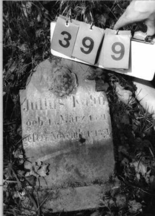 Grabstein 399 (Index: 99792064) Material: Sandstein Zustand: verwittert, Stele liegend Maße HxBxT: 53x32x10 cm Beschreibung: Stele, Sockel, eingezogener Rundabschluß Symbolik: geflügelter Engelskopf Besonderheit: Kindergrab: Grabstein 399