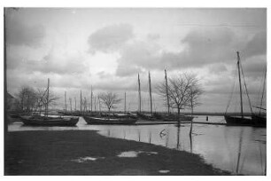 Hafen (an einem Fließgewässer?) mit überfluteten Wiesen. Hinter dem Flachwasser vertäute und verankerte Segelboote