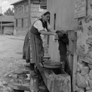 Alltagsbild. Frau in Ihrer Alltagstracht an einer Wasserstelle in Bansko am Fuße des Pirin-Gebirges