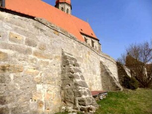Ansicht von Südwesten mit Kirchhofmauer über Feldseite-Im Kern Frühgotisch - Zangenlöcher der Hebezeuge erhalten-mit Strebepfeilern stabilisiert-Wehrgang im 18 Jh abgetragen