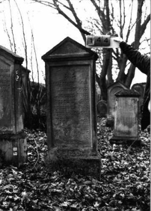 Grabstein 144 (Index: 99751960) Material: Sandstein Zustand: abgeblättert mit Textverlust Maße HxBxT: 160x55x15 cm Beschreibung: Stele, SOckel, Giebel, rechteckiges Schriftfeld eingetieft: Grabstein 144