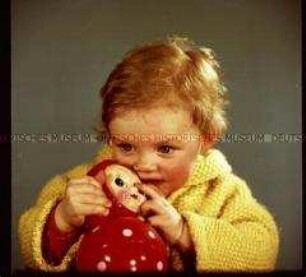Kleines Mädchen mit Strickjacke und Puppe