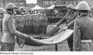 Waren (Müritz). Nationale Volksarmee - Landstreitkräfte. Öffentliche Vereidigung neu in das Panzerregiment 8 (PR-8) einberufener Wehrpflichtiger. Schwursoldaten mit Hand an der entfalteten Truppenfahne und Offizier des Fahnenkommandos (rechts)