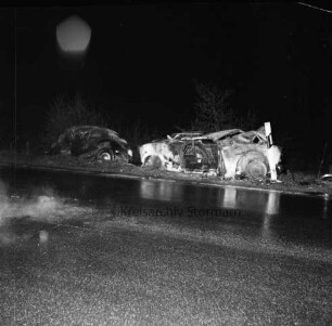 B 404: bei Herrenhaus Nütschau: Verkehrsunfall: Zusammenstoß von zwei Pkws und Auffahrunfall: am Straßenrand zwei ausgebrannte Unfallwagen nach Löschen, Leitpfosten: vorne nasse Fahrbahn: im Dunkeln, 1. Mai 1967
