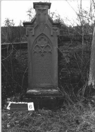 Grabstein 6 (Index: 100114518) Material: Sandstein Zustand: Sockel verwittert Maße HxBxT: 155x55x20 cm Beschreibung: Stele, Sockel, eingezogener giebelartiger Abschluß rechteckig erhöht mit Verdachung, Schriftfeld mit Spitzbogenabschluß Symbolik: Levitenkanne, Maßwerk: Grabstein 6