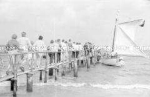 Urlauber auf dem Weg zum Zubringer-Segelboot am Strand Zingst