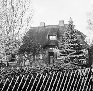 Reetdachhaus, davor Zaun und Garten