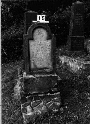 Grabstein 15 (Index: 99802035) Material: Sandstein Zustand: verwittert Maße HxBxT: 148x51x24 cm Beschreibung: Stele, getreppter Sockel, eingezogener Rundbogenabschluß: Grabstein 15