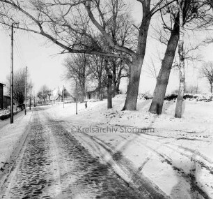 Dorfstraße mit Kopfsteinpflaster in Richtung Neubausiedlung: rechts Baumreihe: dahinter Mitte Kind: hinten links Strommasten und Häuser: Winter
