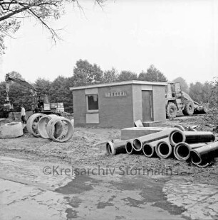 Abwasser: Bünningstedter Straße: Pumpstation: Rohbau: rechts und links davor Rohre unterschiedlicher Größe: hinten rechts Bagger: hinten links zwei Arbeiter vor zweitem Bagger: hinten Bäume