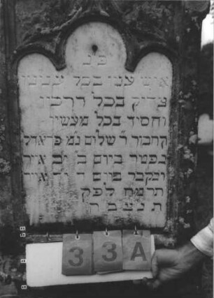 Grabstein 33 (Index: 99800326) Material: Sandstein; Schriftplatte Marmor Zustand: verwittert Maße HxBxT: 188x60x19 cm Beschreibung: Stele mit Mittelerhöhung, Zinnenaufsatz, Schriftplatte eingelassen mit Kleeblattbogenabschluß, getreppter Sockel Symbolik: floral: Grabstein 33A
