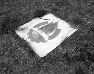 Blechschild (wohl Arbeiter, Bauern, Intelligenz und Jugend betreffend), auf einer Wiese liegend. Muldenhammer-Tannenbergsthal-Gottesberg, ehemaliges Pionierlager "Hanno Günther"