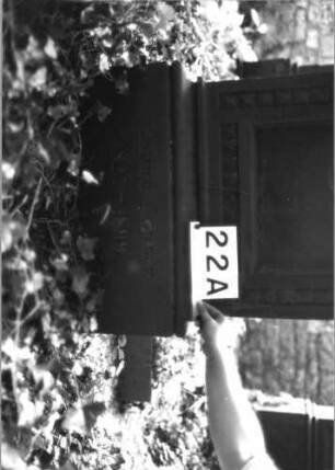 Grabstein 22 (Index: 100081759) Material: Sandstein Zustand: verwittert/abgeblättert am Abschluß Maße HxBxT: 155x54x12 cm Beschreibung: Rundbogenabschl. m. Verdach. , Mittelakroter, Schrift eingetieft, profiliert. Sockel Symbolik: Blätter im Akroter, Diamantfries um Schriftfeld: Grabstein 22A