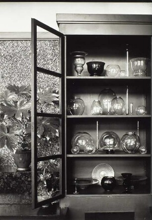 "Blumen um uns" (Photographische Plaudereien in Wort und Bild). Interieur (geöffneter Vitrinenschrank mit Glassammlung und Blumentöpfen)