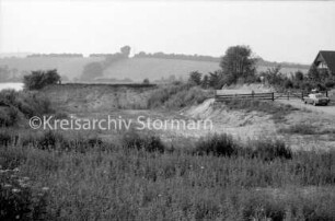 Kieskuhle am Moorteich: rechts Haus: davor Straße mit parkendem Pkw, Tor und Zäunen: im Vordergrund Heide: im Hintergrund der Moorteich und Knicklandschaft: 23. August 1985