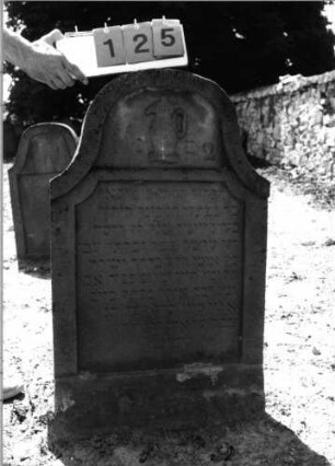 Grabstein 125 (Index: 99798081) Material: Sandstein, rot Zustand: leicht verwittert Maße HxBxT: 102x60x11 cm Beschreibung: Stele, geschweifter Abschluß Symbolik: Levitenkanne: Grabstein 125