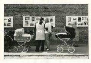 Frauen mit Kinderwagen betrachten eine Fotoausstellung