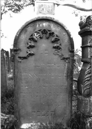 Grabstein 37 (Index: 100103653) Material: Sandstein Zustand: stark verwittert Maße HxBxT: 143x68x12 cm Beschreibung: Stele, Rundbogenabschluss, Schriftfeld eingetieft mit eingezogenem Rundbogenabschluss, im Bogen Maßwerk ( Rundbogenfries) Symbolik: Rundbogenfries: Grabstein 37