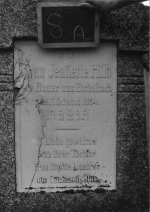 Grabstein 8 (Index: 99936893) Material: Granit, weiße Marmorplatte Zustand: Platte mehrfach gesprungen Maße HxBxT: 189x69x33 cm Beschreibung: konische Stele, Sockel, giebelartiger Abschluß mit Aufsatz, rechteckige Schriftplatte Symbolik: Urnenaufsatz: Grabstein 8A