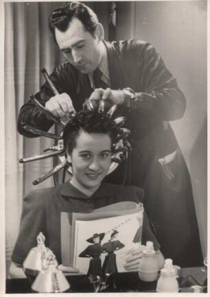 Ein Friseur frisiert eine Frau. Er stellt die Trockenhaube ein