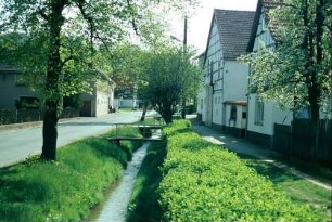 Straße mit parallel fließendem Bach, Häuser, Fußweg, Brücken über den Bach