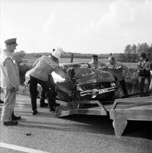 B 208: Kurve bei Westerau: Verkehrsunfall: Zusammenstoß von zwei Pkws: Feuerwehrmänner beim Aufladen von Unfallwagen mit eingedrückter Front auf Plattform von Abschleppwagen: rechts Zuschauer: Zaun, hinten Feld, im Hintergrund Wald
