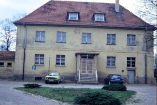 derzeit noch genutztes Schulgebäude; davor Freifläche mit Grünanlage