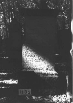 Grabstein 1133 (Index: 99899829) Material: Sandstein Zustand: stark verwittert Maße HxBxT: 145x66x25 cm Beschreibung: aufgesockelte Stele mit Verdachung, in den Ecken Blüten Symbolik: Blüten Besonderheit: kulturhistorisch wertvoll / hist.-wiss. Gründe (Gemeindestellung): Grabstein 1133