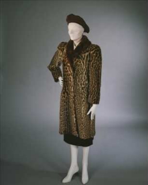 Leoparden-Mantel, cremeweiße rückenfreie Wickelbluse, schwarzer schmaler Rock und schwarzes Filzbarett (Archivtitel)