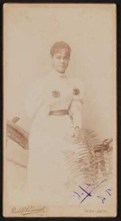 Elisabeth (Lisl) Nicolics im weißen Kleid, an ein Holzgeländer lehnend, davor ein Farn, mit Widmung