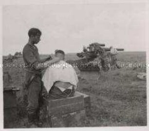 Wehrmachtssoldaten, Soldaten in Rußland, Gefechtspause bei der schweren Artillerie, In nächster Nähe der 15-cm-Haubitze waltet der Batterie-Friseur seines Amtes.