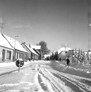Segeberger Straße: vorn links Verkehrsinsel mit Straßenschild: rechts auf Fußgängerweg Frau mit Kinderwagen: dahinter Mann: rechts und links Wohnhäuser: hinten Pkw: Winter