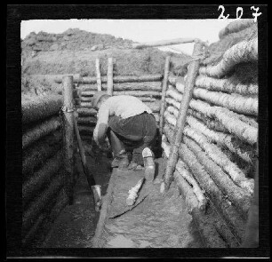 Komaika-Stellung (=Kamaja/Kamoja, Gewässer in Litauen): Soldat bei Bodenarbeiten in einem Laufgraben ("Stellungsbau in der Komaika-Stellung") (Rückansicht)