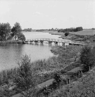 Herrenteich: Fischhuser Damm: hölzerne Fußgängerbrücke: Blick Richtung Nordosten auf oberen Herrenteich: im Vordergrund Ufer mit Schilf, Büsche, Zaun, Wanderweg