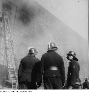 Berlin (West). Brandbekämpfung in einem Lagergebäude. Einsatzkräfte in Bereitschaft vor ausgefahrener Drehleiter