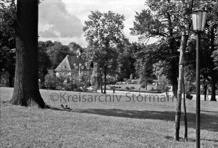 Kurpark: Blick vom Kurparkhügel mit Bäumen auf Rondeel am Sülzberg mit Bänken, Rabatten und Hecken: hinten links Haus des Handwerks: vorn rechts Laterne: im Hintergrund Bäume