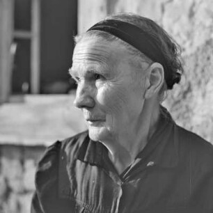 Strohgedecktes Blockhaus in Burg-Kauper. Frau Nowick in Spreewälder Alltagstracht vor ihrem Gehöft. : Ze słomu skryte kładźity twar statoka w Kupaŕskich Bórkowach. Knjeni Nowickowa we wšědnej Błótowskej drasće před swojim statokom.