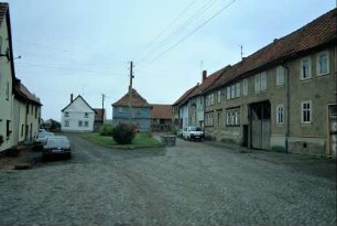 Straßengabelung mit platzartiger Erweiterung und Grünfläche; beiderseits Gehöfte