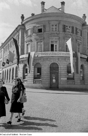 Mit Fahnen und Bannern geschmücktes Gebäude, im Vordergrund weibliche Mitglieder der FDJ