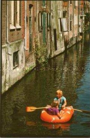 Kinder fahren mit einem Schlauchboot einen Kanal entlang (Altersgruppe 18-21)