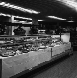 Peters Delikatessen: Mühlenstraße, Ecke Hindenburgstraße: Feinkostgeschäft: 50-jähriges Firmenjubiläum, gleichzeitig Betriebsübergabe: Innenaufnahme: Verkaufsraum: Buffet, Platten mit Speisen auf Tischtüchern: Blumenschmuck